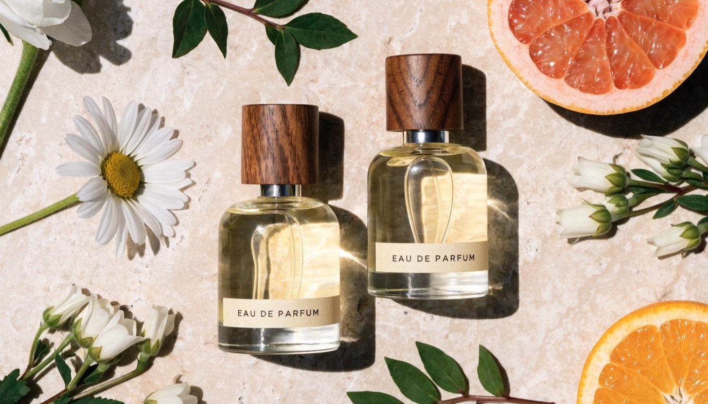 Natural perfume bottles with fresh flowers, citrus, and herbs on a stone surface against a bright background