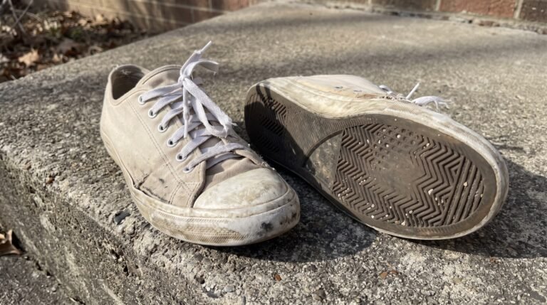 A worn pair of white sneakers side by side on a pale concrete step in bright directional daylight