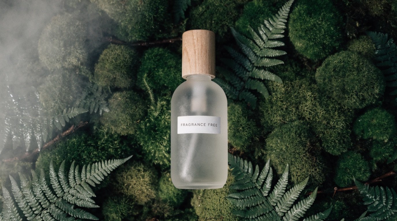 A frosted glass bottle with a wooden cap labeled Fragrance Free, laid on a bed of deep green moss and ferns and shot from above in soft misty light