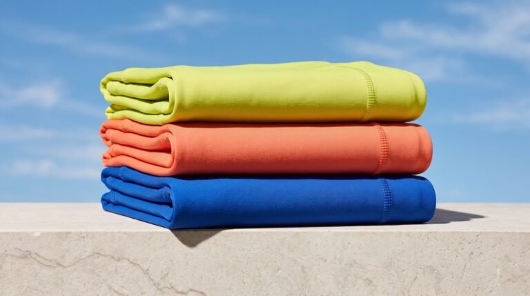 Folded recycled-polyester leggings in bright colors stacked on a pale stone ledge against a clear blue sky