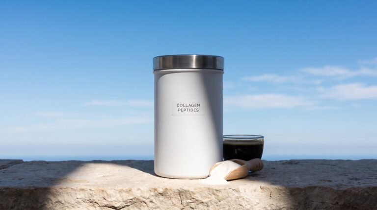 A matte white canister labeled collagen peptides on a sunlit stone ledge beside a wooden scoop of white powder and a small glass of black coffee, against open blue sky