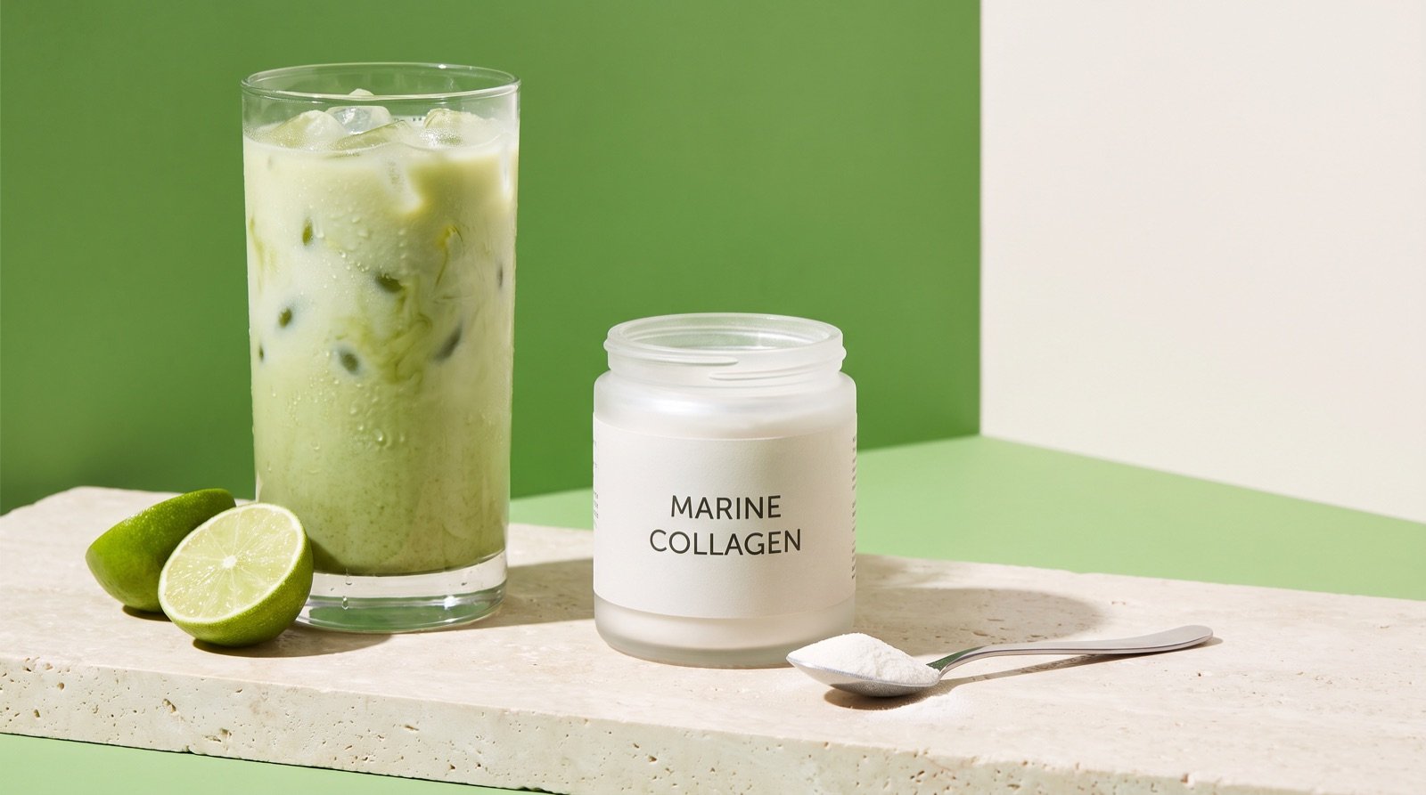 A tall glass of iced matcha latte next to a frosted jar labeled marine collagen and a teaspoon of powder on a stone ledge, against a bright green background