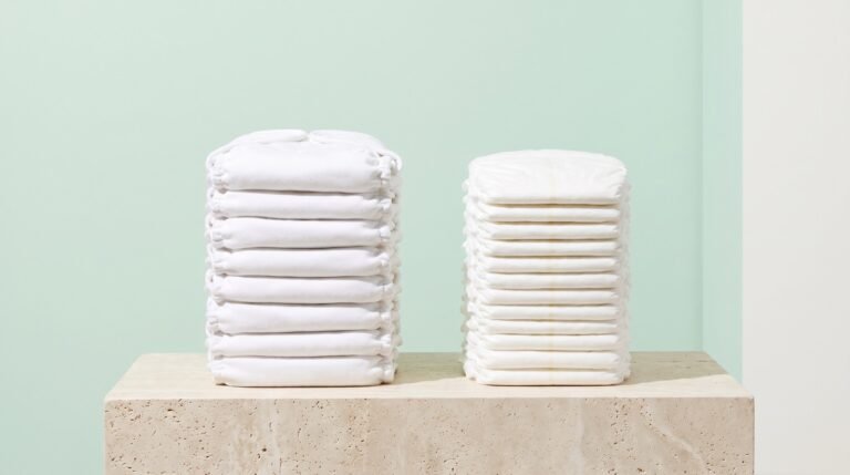 Folded cloth diapers beside natural disposable diapers on a bright neutral surface