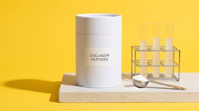 A white canister labeled collagen peptides on a stone plinth beside a rack of three glass test tubes and a steel scoop, against a bright yellow background